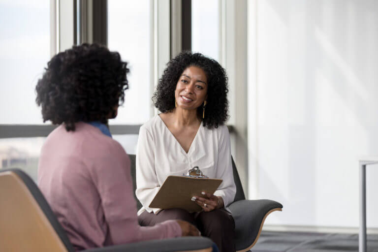 A bipolar disorder specialist talking to her patient while writing notes down on a clipboard.